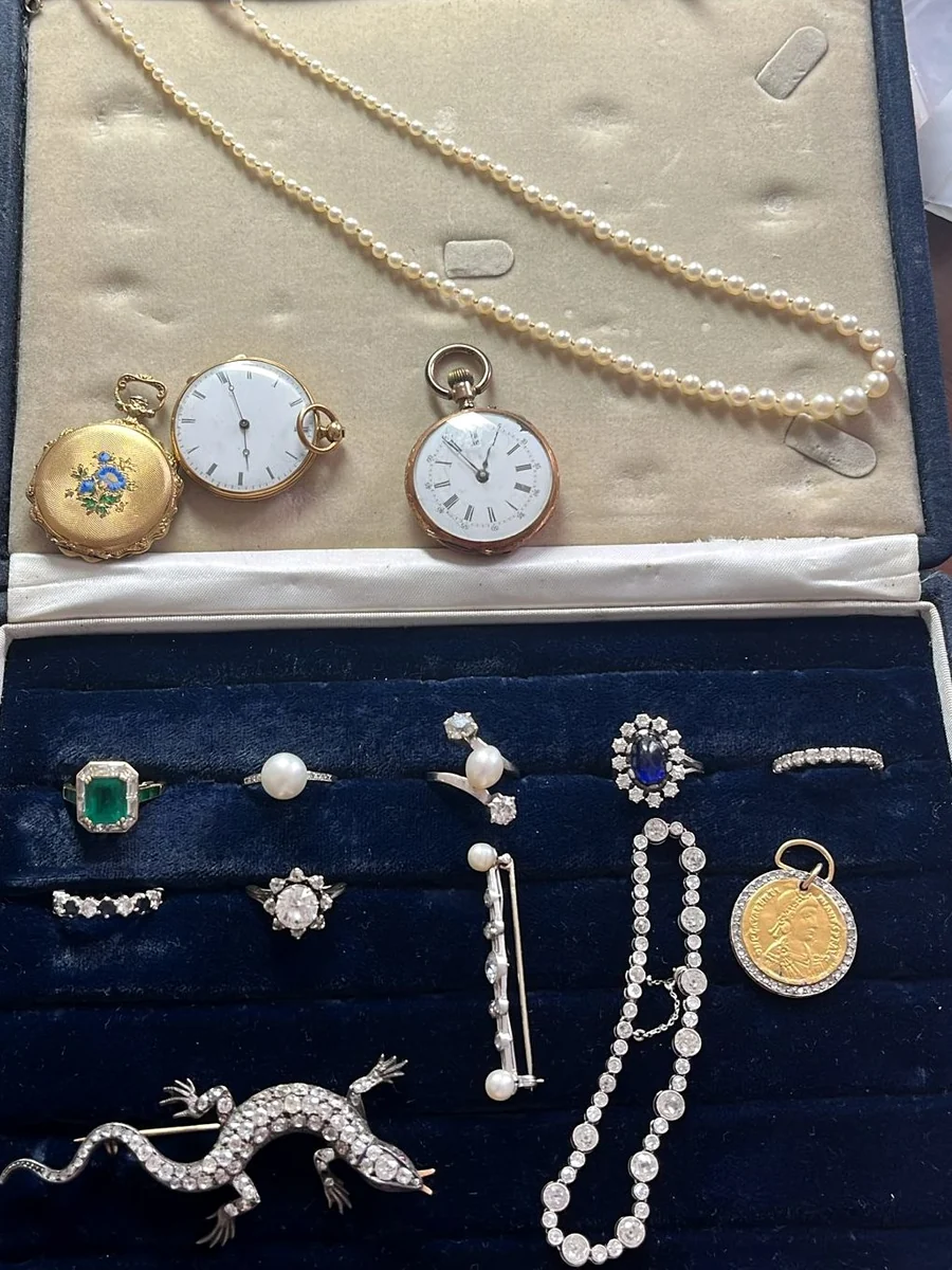 Un écrin de famille ouvert : collier de perles, montres de gousset, bagues, broche lézard, bracelet de diamants